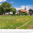 Mai 2027 Kalenderansicht. Blühende Wiese vor traditionellen Gebäuden unter blauem Himmel.