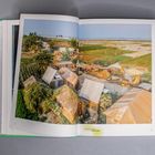 Text: "AWARD RECIPIENT KHUDI BARI". Gezeigt wird eine ländliche Siedlung mit einfachen Hütten und umliegenden Feldern.