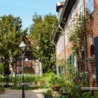 "Lübeck II: Auf verschlungenen Wegen zum Domviertel" und "Eines von 90 kleinen Paradiesen: der Haasenhof". Zwei rote Backsteinhäuser, gepflasterte Gasse, viel Grün.