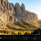 "Mai, Dolomiten Kalender. Majestätische Felswände im Sonnenlicht, grünes Tal unten, Bäume verstreut."
