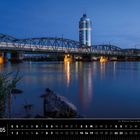 "Wien 05. Der Millenium Tower an der Donau in der blauen Stunde. Ein beleuchteter Turm und Brücke spiegeln sich im Wasser."