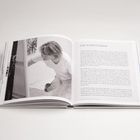 Text: "DIE KÜNSTLERIN"

Aufgeschlagenes Buch mit Schwarz-Weiß-Foto einer Frau, die sich über eine Leinwand beugt.