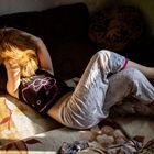 Eine Person in bequemer Kleidung liegt auf einem Sofa mit einem Hund, Sonnenlicht fällt darauf.
