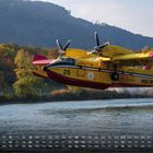 Kalender im Mai, Wochenanfang Samstag. Löschflugzeug "VIGILI DEL FUOCO" fliegt knapp über Wasser vor einer herbstlichen Landschaft.