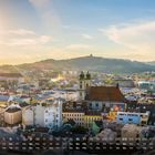 Kalender mit Mai-Daten unten; Stadtansicht von Linz mit Sonne, Kirchen und Hügeln im Hintergrund.