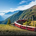 Kalender mit Mai-Woche 1-5. Roter Zug windet sich durch alpines Tal mit grünen Hängen und blauen Bergen.
