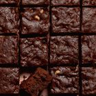 Schokoladenbrownies in gleichmäßigen Quadraten angeordnet, einer teilweise herausgenommen. Einladendes Muster.