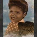 Text: "GLANZ". Eine Frau mit großem Haar und Polka-Dot-Kleidung vor einem himmlischen Hintergrund mit Flügeln und Sternen.