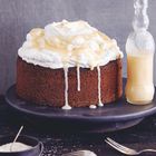 Dunkler Kuchen mit Sahne und Vanillesauce. Daneben eine Glasflasche mit Vanillesauce. Auf einem Tisch mit Besteck.