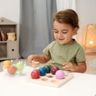 Ein Kind spielt mit bunten Holzkugeln an einem Tisch, im Hintergrund ein Regal mit Spielzeug und Bücher.