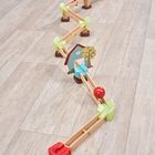 Eine Holz-Murmelbahn mit bunten Elementen; Bäume, Haus und Regenbogenmuster. Plaziert auf einem Holzboden.