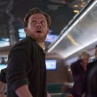 Keine sichtbaren Texte vorhanden. Ein Mann mit Bart blickt beeindruckt nach oben in einem modernen Innenraum mit Menschen im Hintergrund.