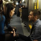 Eine Frau in blauem Pullover spricht mit einem sitzenden Mann in einem grauen Hemd in einem Zugabteil.