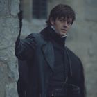 Ein Mann in dunkler Kleidung lehnt an einer Steinmauer und blickt seitlich in die Ferne. Die Stimmung ist düster.