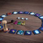 Spielbrett mit Karten im Kreis, Sanduhr, schwarzen Würfel, bunten Spielsteinen und Jetons auf Holzuntergrund.