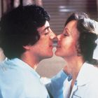 Ein Mann und eine Frau in blauer Kleidung stehen nah beieinander und nähern sich für einen Kuss.