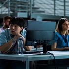 Eine Gruppe junger Menschen sitzt an Computern in einem modernen Raum mit Kopfhörern, konzentriert und aufmerksam.