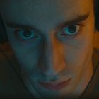 Ein junger Mann trägt Kopfhörer und schaut intensiv nach vorne. Sein Gesicht ist teils in blaues Licht getaucht.