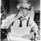 S/W-Bild: Mann mit Brille raucht, hält Papier, zwei Mikrofone. Bücherregal im Hintergrund, klassische Büroeinrichtung.