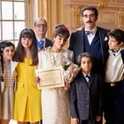 Eine Frau in der Mitte hält ein Blatt Papier mit Text. Sie ist von fröhlich wirkenden Menschen in eleganter Kleidung umgeben.