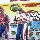 Verschiedene Rennfahrer in bunten Overalls stehen vor Logos von "NASCAR", "Advance Auto Parts" und "Martinsville Speedway".