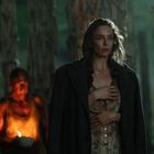 Eine Frau steht im Wald, wirkt nachdenklich. Hinter ihr ein beleuchteter Mann mit einer Schale in der Hand.