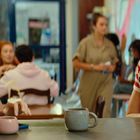 Zwei Männer in gestreiften T-Shirts sitzen in einem Café und unterhalten sich. Um sie herum sitzen weitere Personen.