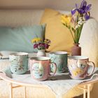 „Kleine Auszeit“, „Zeit für mich“; Pastellfarbene Tassen mit floralen und Schmetterlingsmustern, Blumen im Hintergrund.