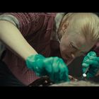 Ich sehe keinen Text. Eine Person mit blonden Haaren untersucht konzentriert etwas, trägt grüne Handschuhe und hält eine Lampe.