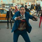 Digitale Anzeige zeigt 09:59:10. Mann in blauem Anzug wirkt panisch, umgeben von aufmerksamen Menschen auf der Straße.