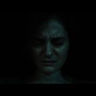 Frau mit geschlossenen Augen, wirkt angespannt, der Hintergrund ist dunkel und kaum sichtbar.