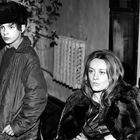 Zwei Personen in Winterkleidung in einem Raum. Der Junge trägt eine Fellmütze, die Frau sitzt in einem Stuhl.