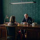 Ein Mann und eine Frau sitzen sich in einem Bürozimmer an einem Holztisch gegenüber.