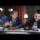 Drei Männer an einer Bar: einer trinkt mit Sonnenbrille, ein anderer hat ein Bier, und der dritte lacht mit einem Getränk.