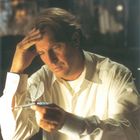 Texte: www.im_zeichen_der_libelle.de, www.movie.de. Ein Mann in einem weißen Hemd betrachtet nachdenklich eine Libellenfigur.