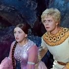 Ich kann keine Texte oder spezifischen Details erkennen. Zwei Menschen schauen überrascht, in einem dunklen, steinigen Umfeld.