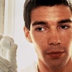 Ein Mann in weiß hält einen Golfball mit Handschuh, schaut konzentriert.