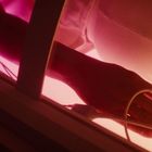 Ein Arm liegt in rosafarbenem Licht, mit einem Clip am Finger und Kabeln, die über den Arm verlaufen.