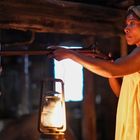 Keine Texte. Eine Frau in Nachthemd und Kopftuch hält ein Gewehr, neben einer brennenden Laterne im dunklen Raum.