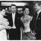 Zwei Männer und zwei Frauen in eleganter Kleidung, in einem feierlichen Ambiente aus der Vergangenheit.