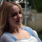 Keine sichtbaren Texte. Eine lächelnde Frau mit blondem Haar sitzt entspannt in einem hellen Raum.