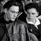 Eine Frau und ein Mann sitzen eng beieinander, schauen ernst und wirken nachdenklich. Schwarz-weiß Fotografie.