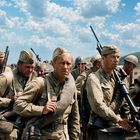 Soldaten in staubigen Uniformen mit Gewehren marschieren unter einem blauen Himmel mit Wolken.