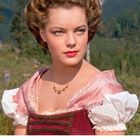 JUNI-Kalenderseite, Bild einer Frau in traditioneller Kleidung, elegante Frisur, grüner Wald im Hintergrund.