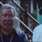 Es sind keine Texte oder Logos vorhanden. Ein älterer Mann mit Brille und grauen Haaren steht neben einer Treppe.