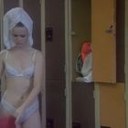 Eine Frau in Unterwäsche mit Turbanhandtuch steht neben geöffneten Spinden in einer Umkleidekabine.