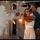 Keine Texte. Ein Mann und eine Frau stehen erschrocken bei einem großen Funkenflug, der von einer Pistole ausgeht.