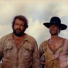 Zwei Männer stehen nebeneinander, einer mit Vollbart in zerknittertem Hemd, der andere trägt einen Stern und einen schwarzen Hut.