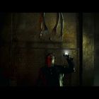 Keine Texte. Eine Person hält eine Taschenlampe in einem dunklen Raum; über ihr hängen lange, knochige Arme von der Decke.