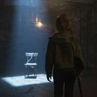 Ein Raum mit karger Beleuchtung, ein leerer Holzstuhl mit Kette im Lichtkegel. Eine Person im Hintergrund.